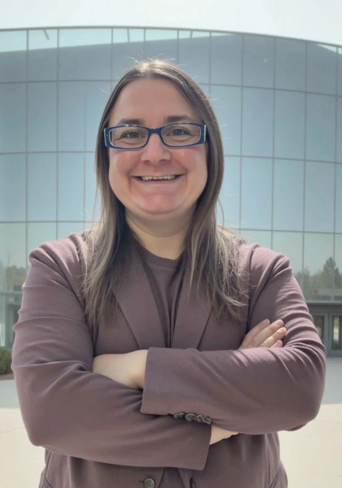 Hillary Ramsey, founder of RFIP Analytics, smiling with arms crossed outside a modern glass building